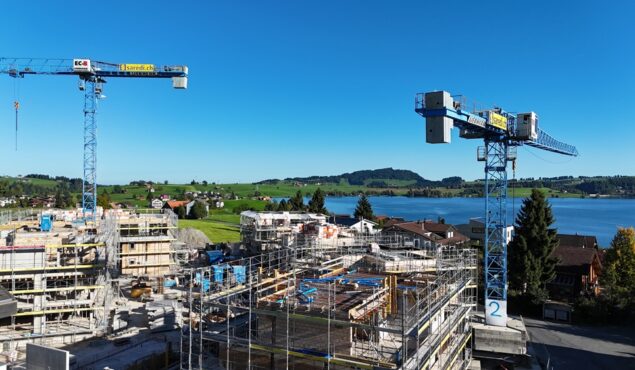 Baustelle mit Kränen am Seeufer unter blauem Himmel