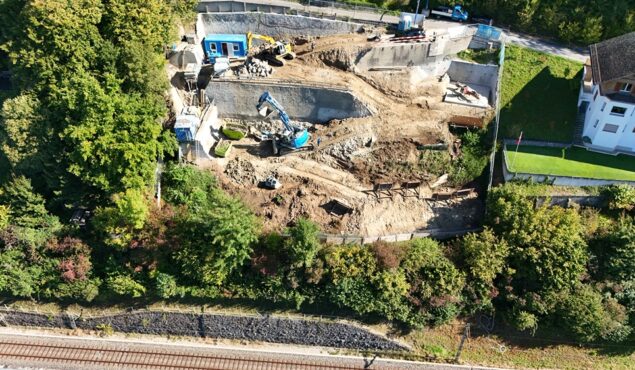 Baustelle mit Baggern neben Wohnhaus und Bäumen