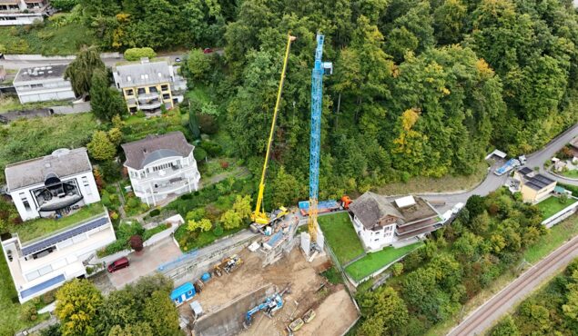 Baustelle mit Kran neben Wohnhäusern und Waldgebiet