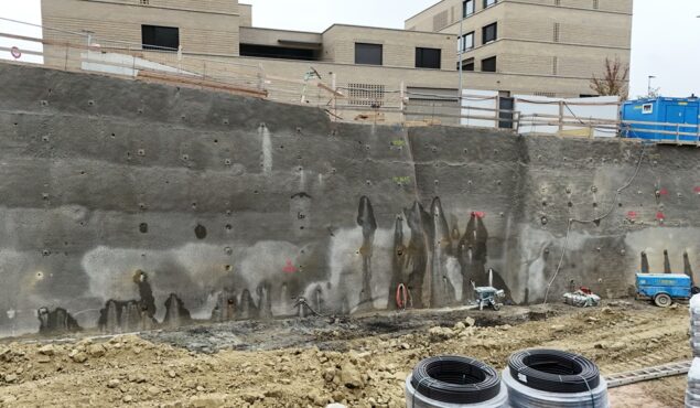 Baustelle mit Spritzbetonwand und Gebäuden im Hintergrund